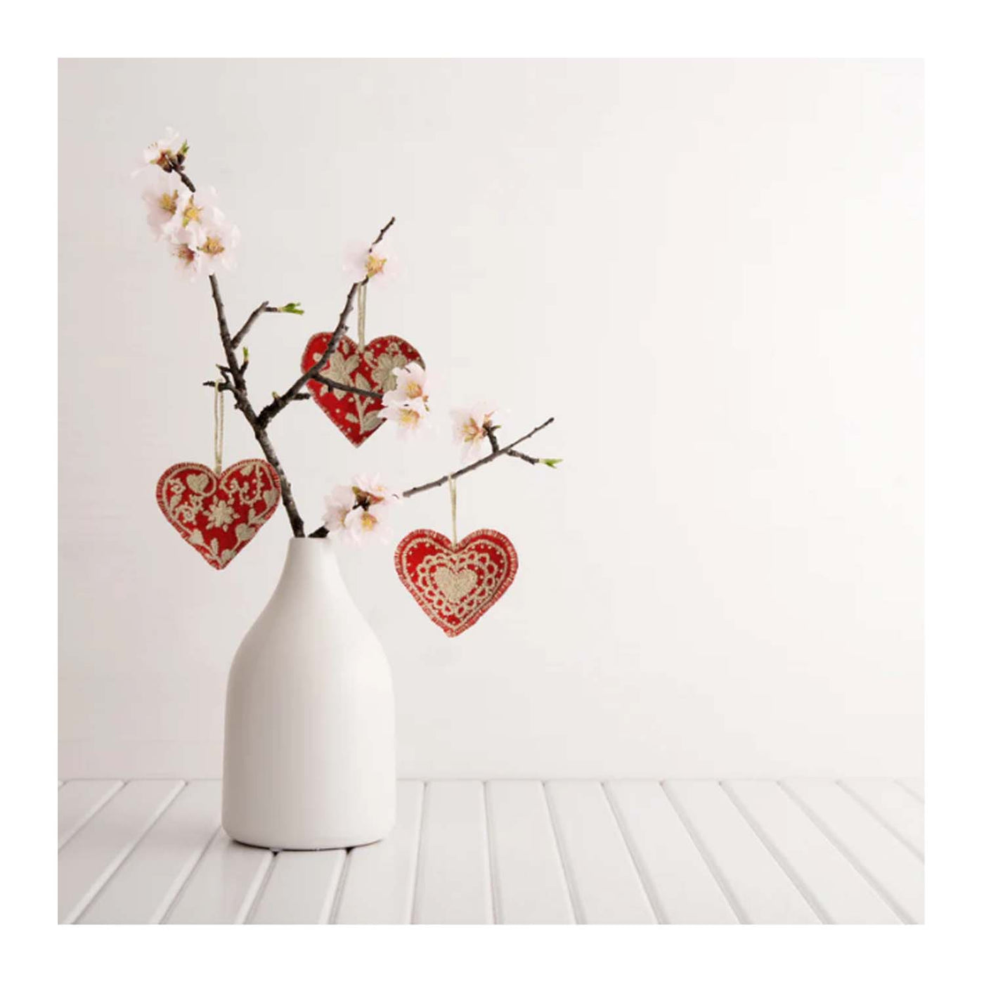 embroidered hearts hanging from branches in a vase