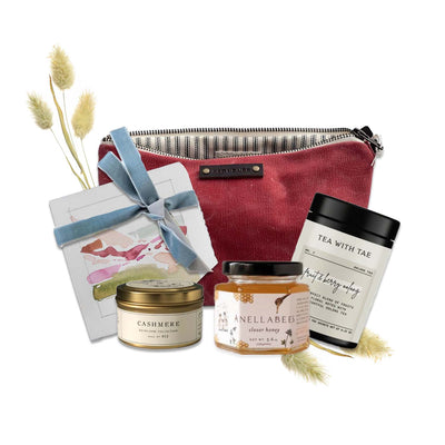 red waxed canvas pouch, jar of raw clover honey, container of tea, cashmere scented candle, and landscape card pack